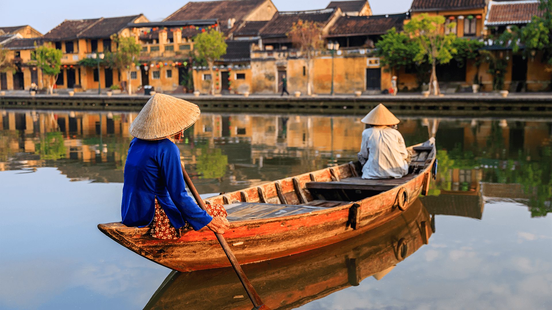 Two people in conical hats paddling a wooden boat 
