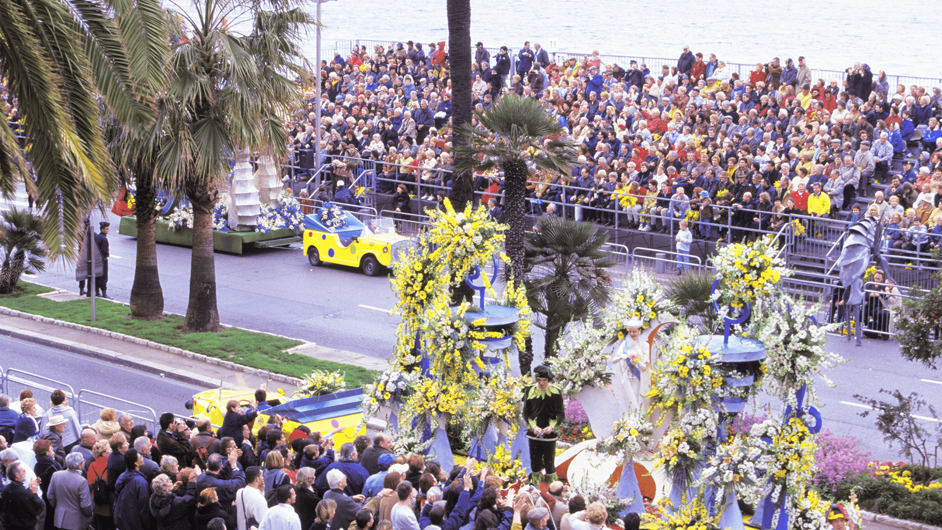 Crowds line a seaside street watching floats pass by