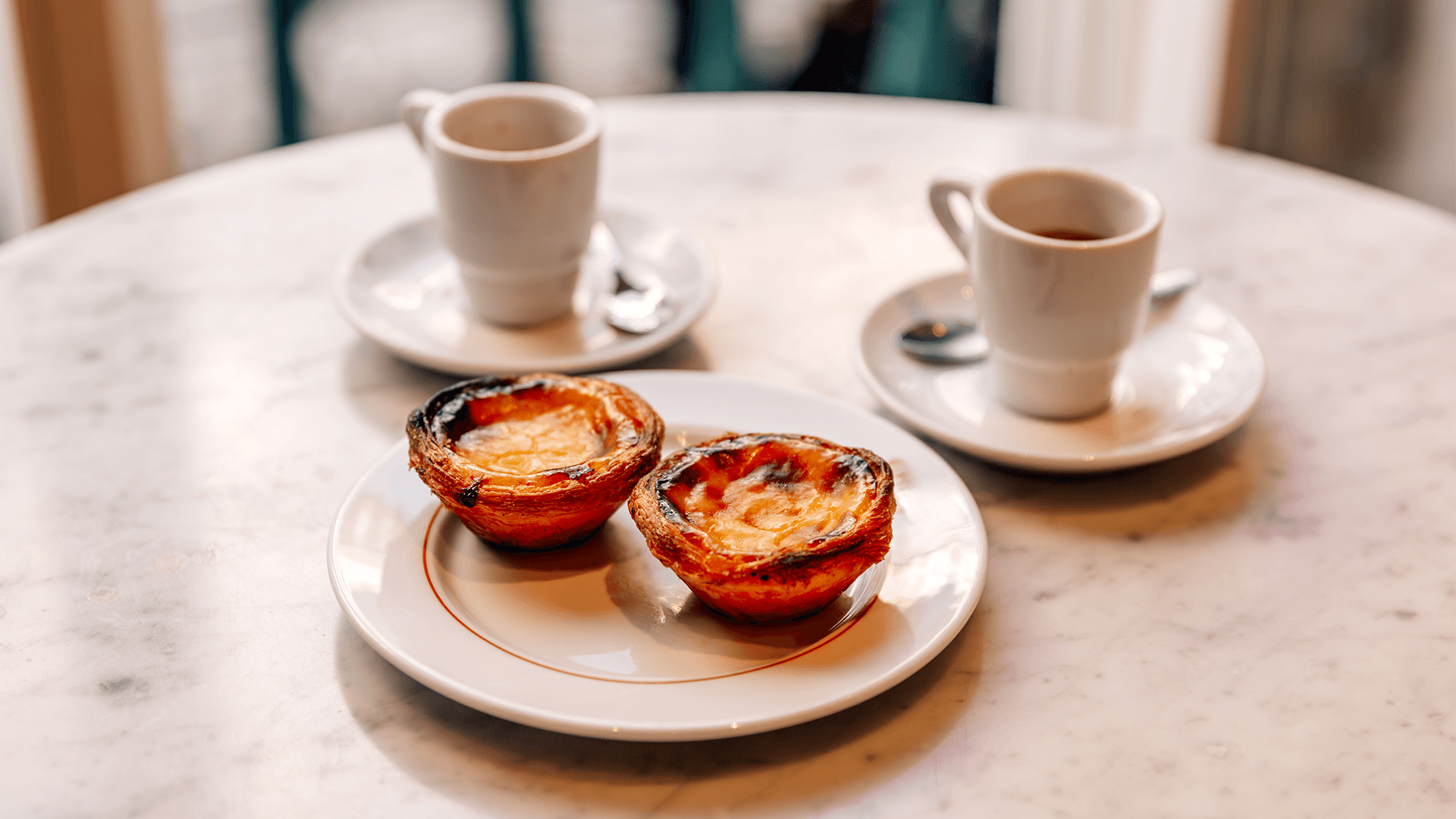 Two pastel de nata and two cups of espresso on a table