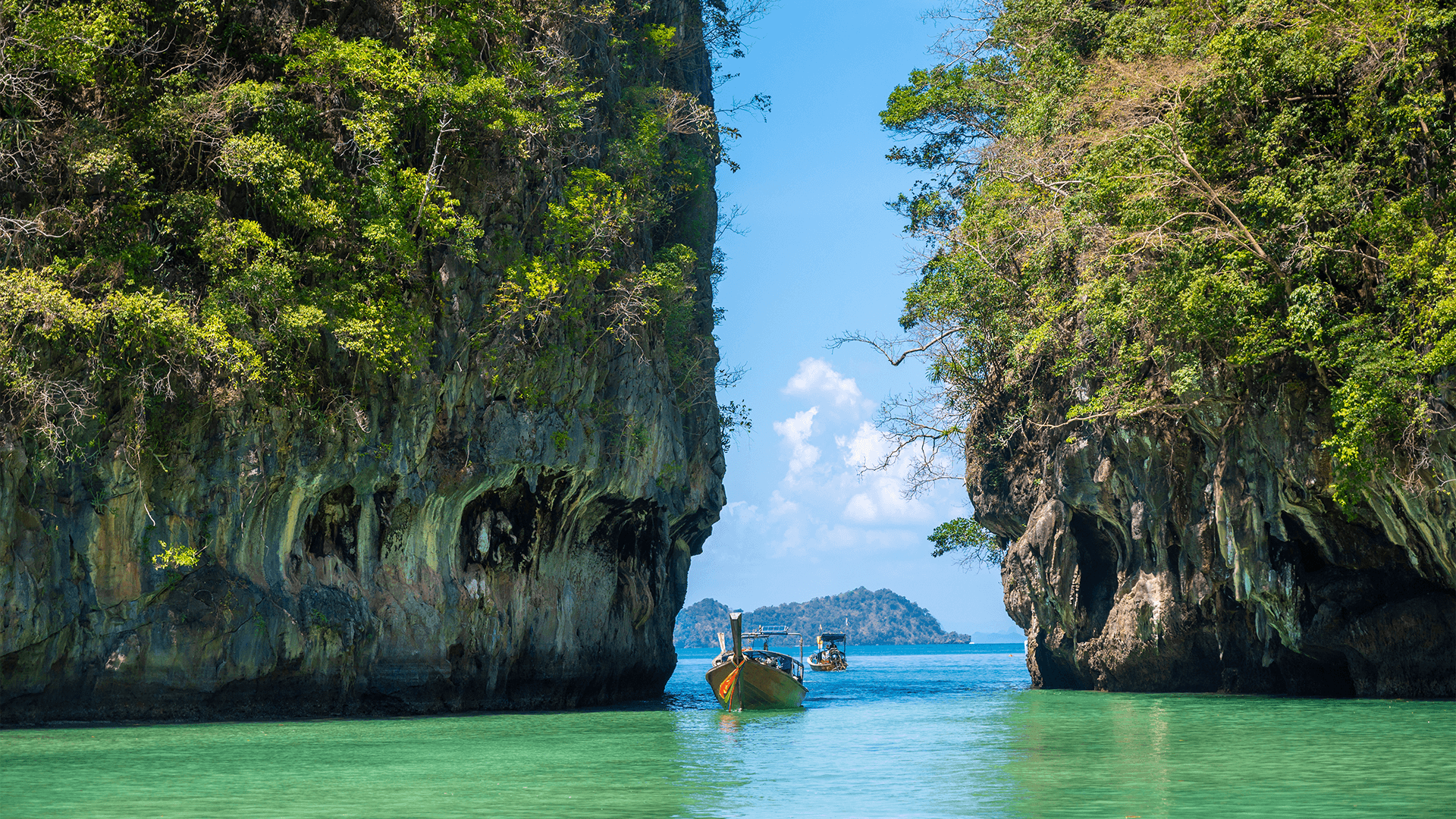 Wooden boats sail between towering green islands