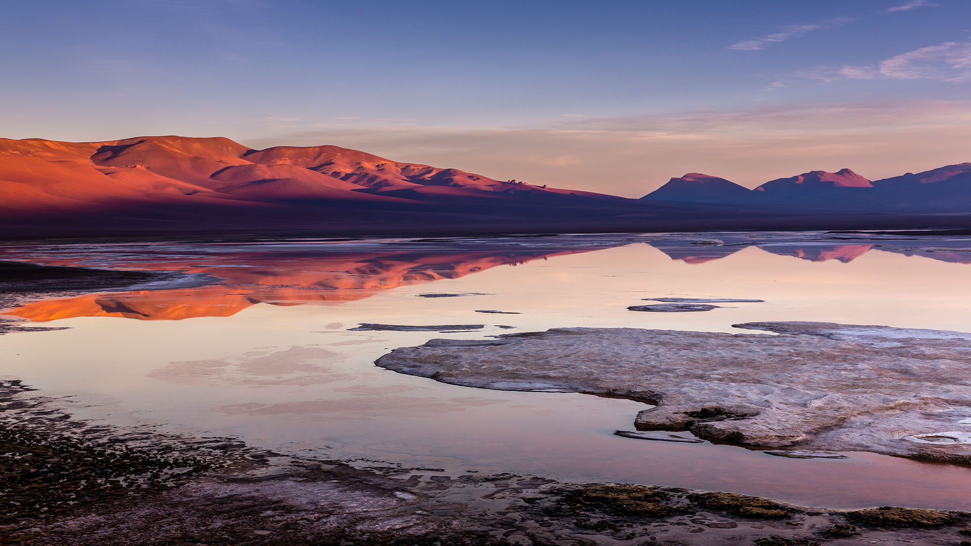 Salt flats reflecting desert mountains at sunset
